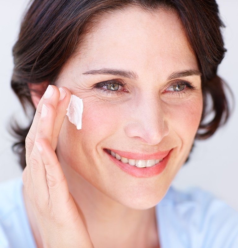 Eine Frau trägt Creme auf ihre rechte Wange auf